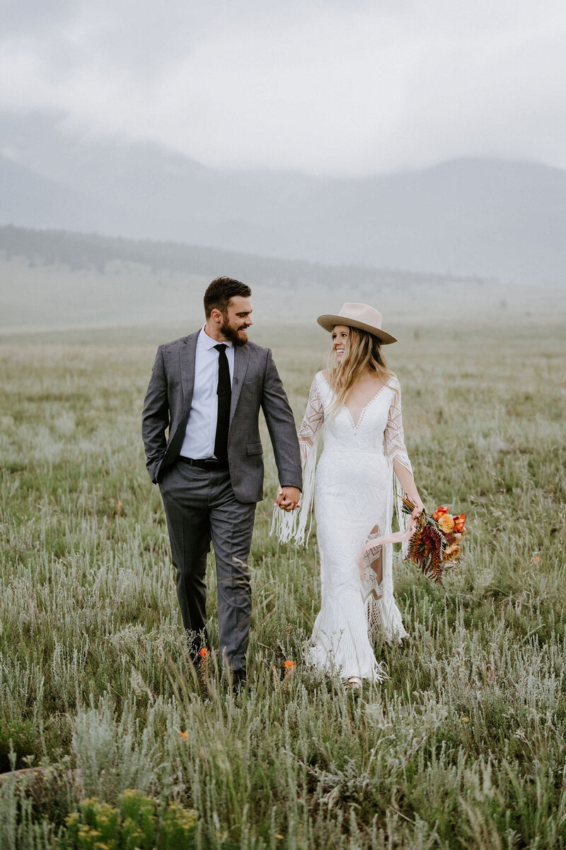 bride and groom holding hands in field in Colorado during wedding