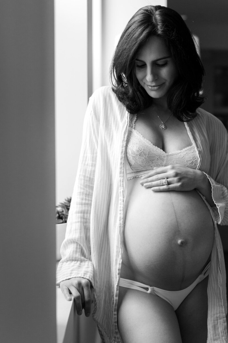 A black and white photo of a pregnant woman looking down at her baby bump