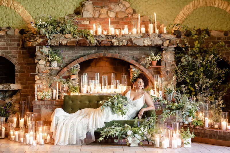 bride sits in front of brick fireplace with candles and greenery