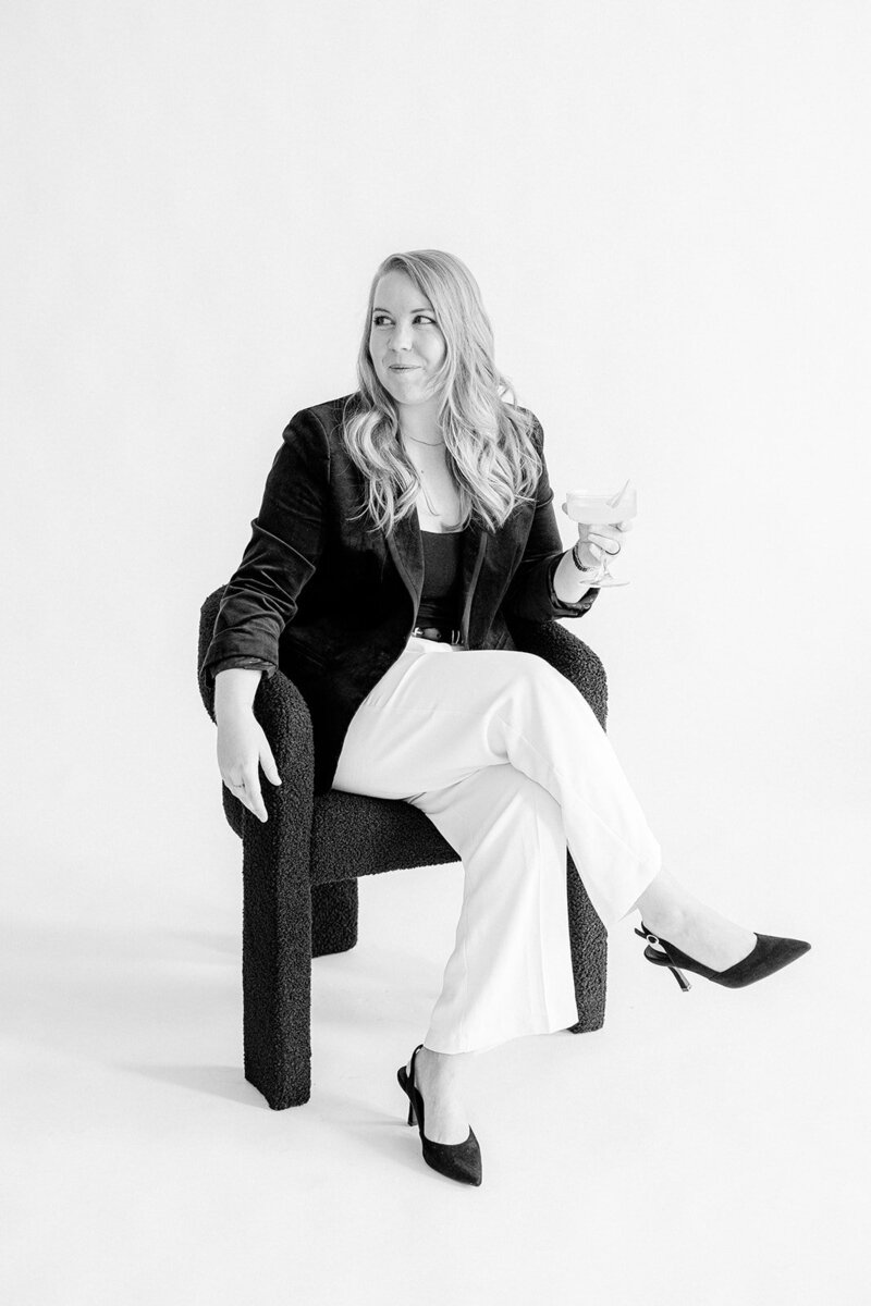 Lizzy Grant sitting in chair with blazer and heels looking off camera