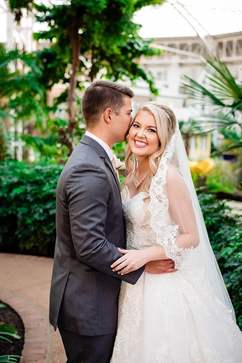 Bride smiling at camera as her husband whispers in her ear, inside Gaylord Opryland