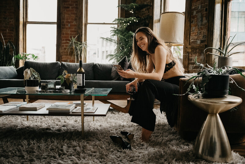 Showit websites designer, Clair Schwem, working on her phone on a luxury branding project. She is stilling in a living room with a brick wall in the background surrounded by plants.