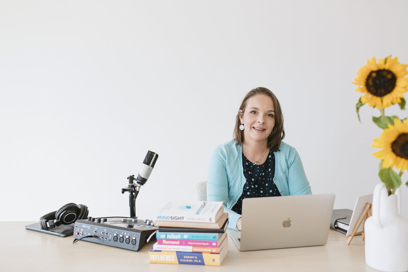 Image of Emily May at her desk with Podcast  laptop and books