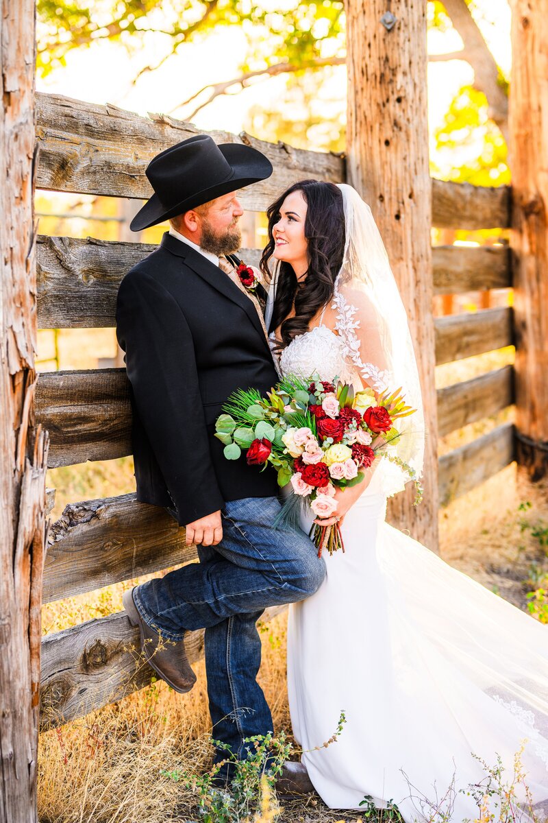Flagstaff wedding bride and groom looking at each other leaning on wooden fence bride holding bouquet at Historic Hat Ranch Williams Flagstaff Julia Romano Photography