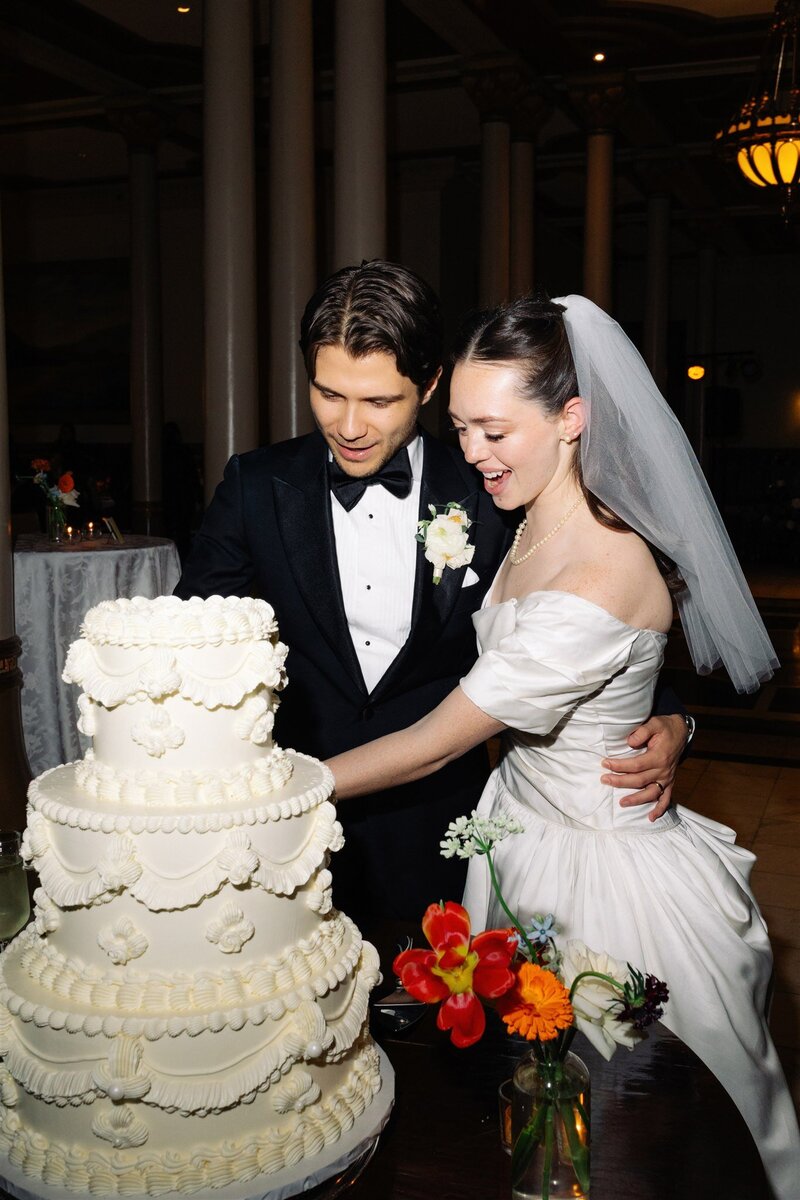 Bride and groom cutting a vintage-style white wedding cake during their Austin reception, planned with charm and attention to tradition.