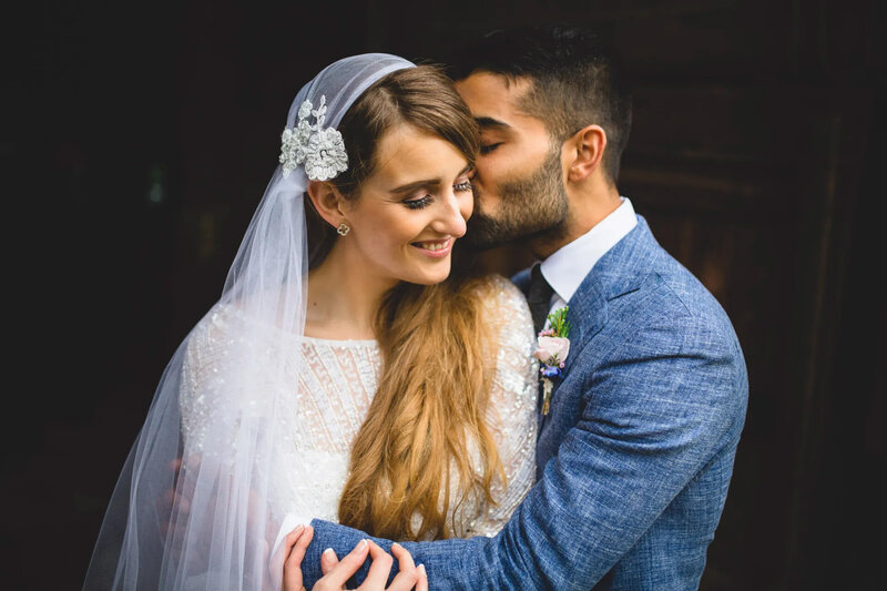 groom kissing the cheek of the bride at east riddlesden hall in yorkshire