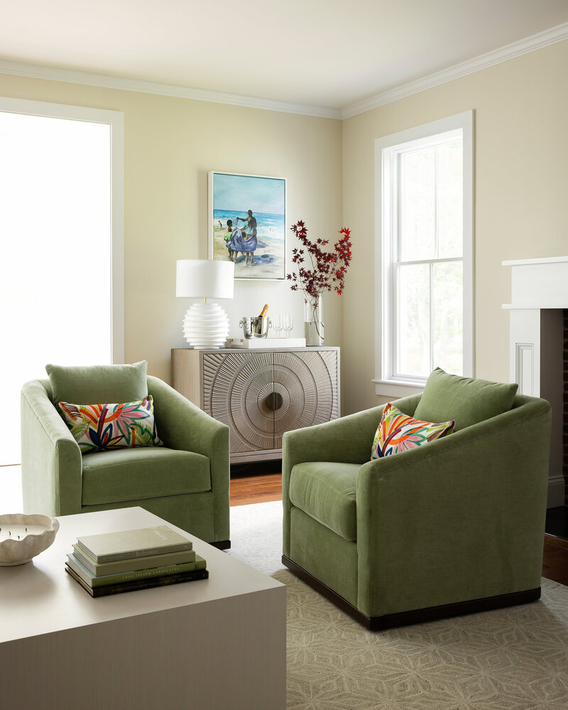 Inviting living room with green armchairs, a wooden coffee table, large windows letting in natural light, and a vase with flowers on the table