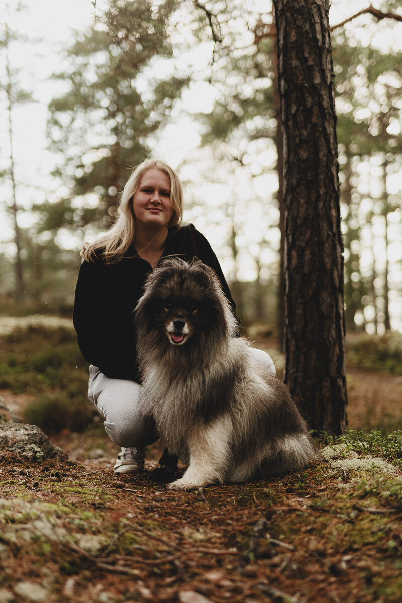 Ett porträtt på fotografen Fia Wolle tillsammans med hennes hund Kito sittandes i skogen i Stockholm