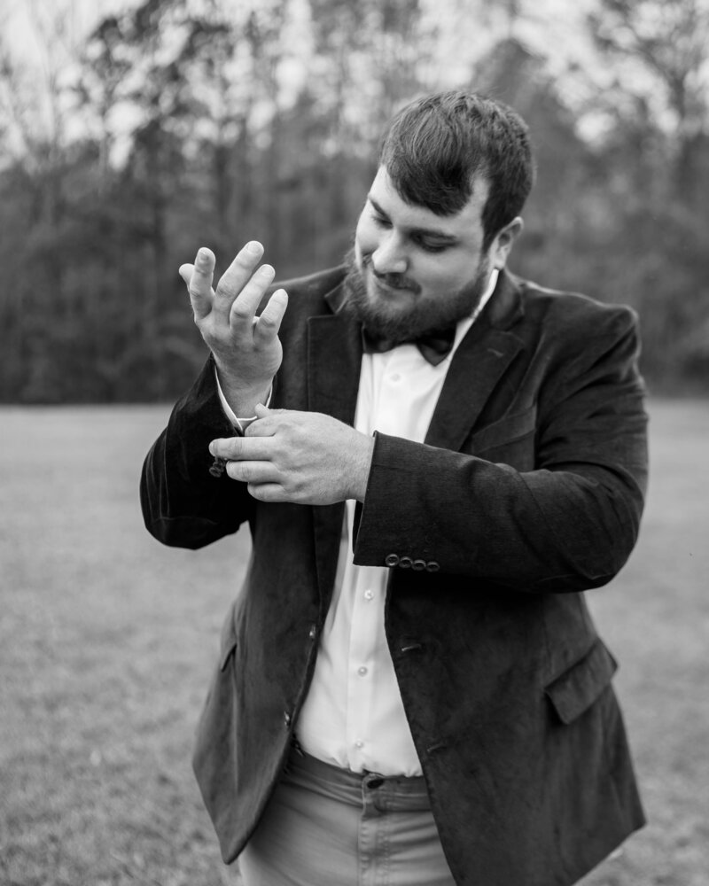 Groom standing in a field buttoning his shirt.