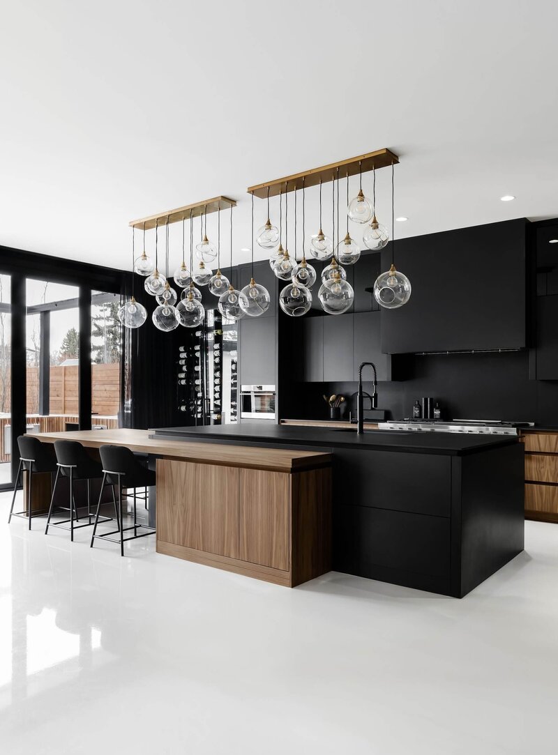 A bold dramatic kitchen with black dekton and walnut features and oversized pendant glass lighting. 