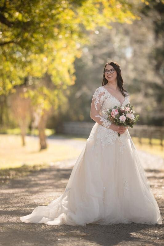 bride wearing glasses and a wedding dress poses on her wedding day holding a bouquet of flowers