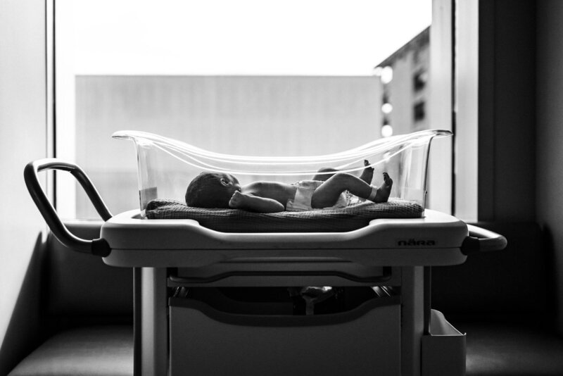 newborn in diaper laying in hospital bassinet in front of window
