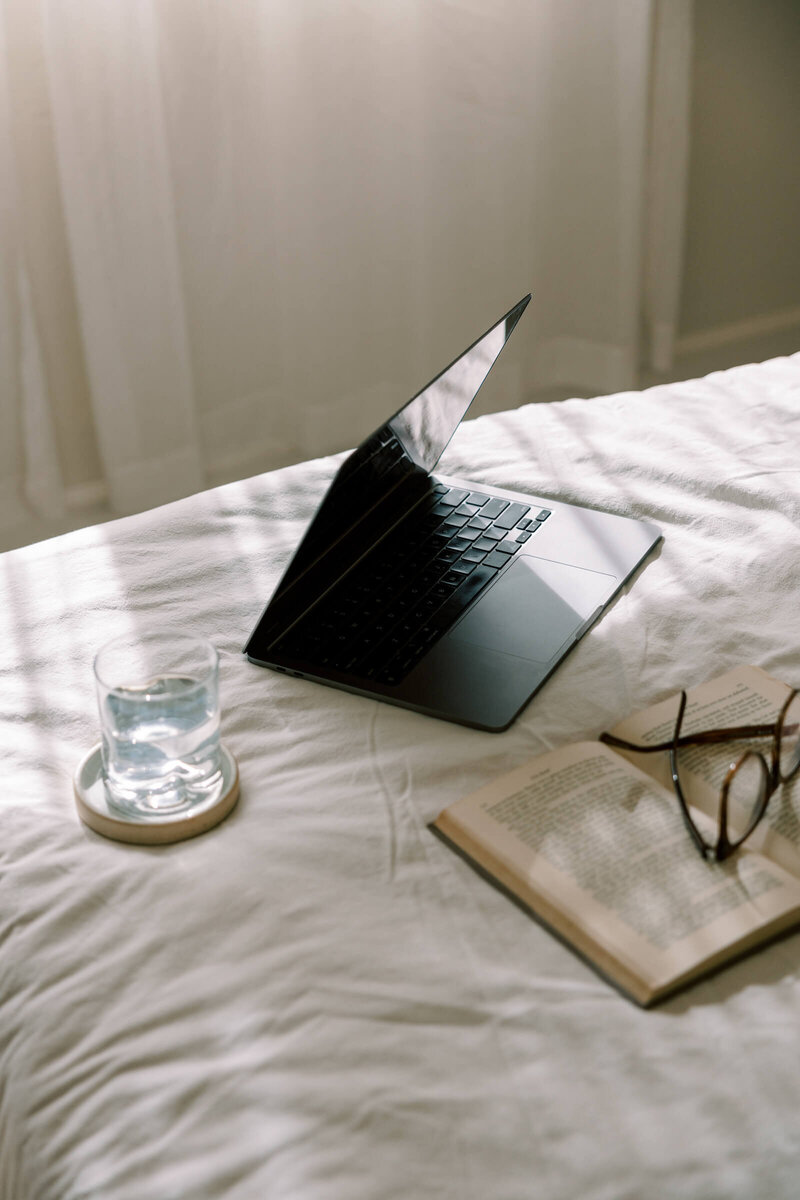 Individual reclining on a bed, engaged with a cell phone. A white canvas tote bag with the text "LES BASICS" hangs on the chair, perfect for carrying showit template customization notes.