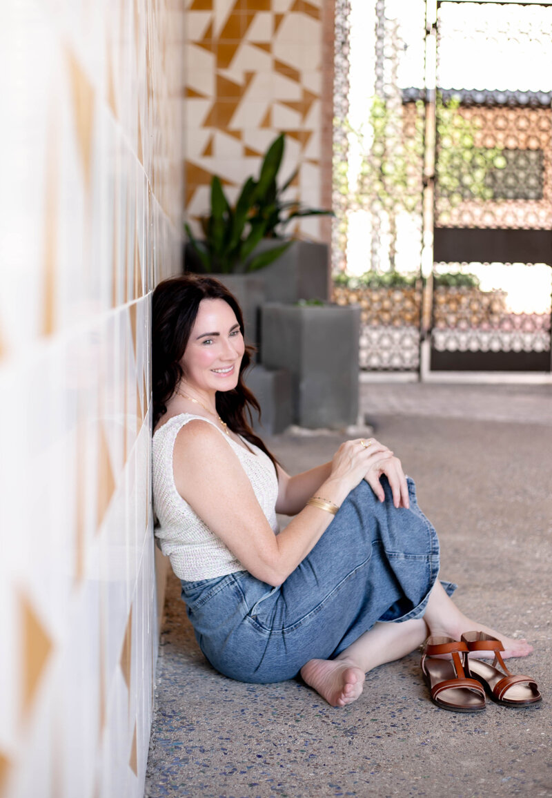 Trish, holistic nutritionist, yoga teacher, and breathwork coach, sitting on the ground looking away smiling