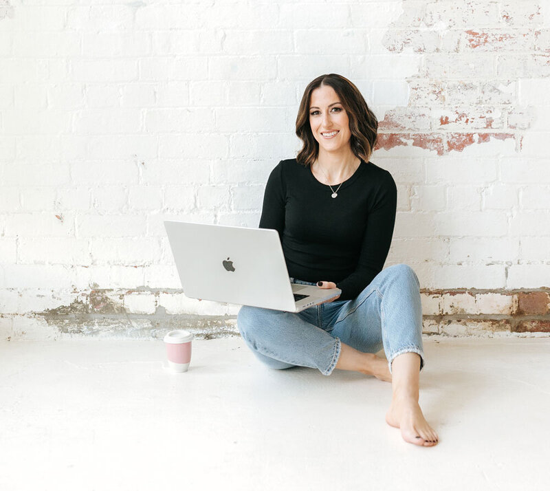 Founder Kristy sitting on floor in front of white wall with laptop on lap