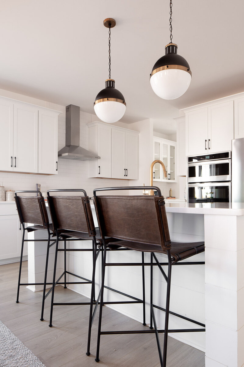 Kitchen counter with dark leather chairs. White kitchen with golden faucet
