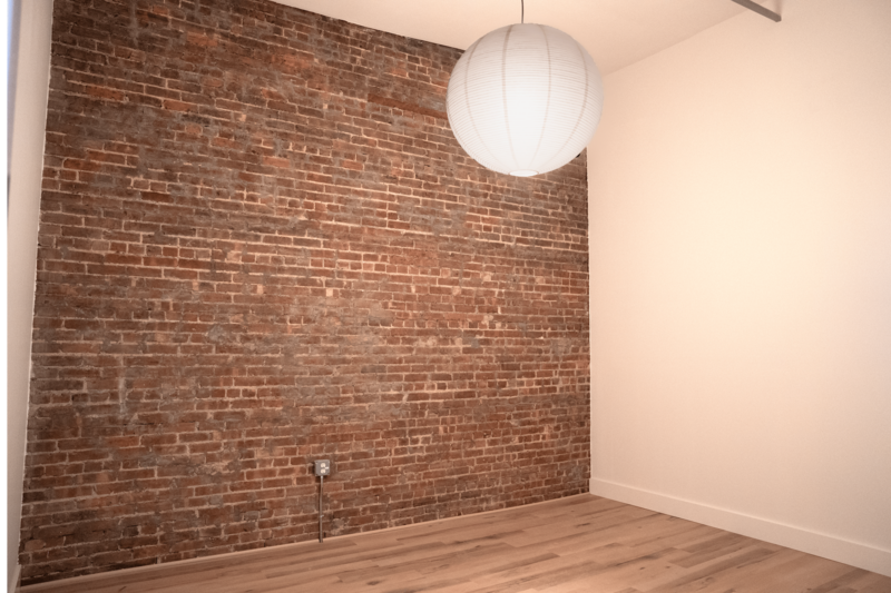 Large unfurnished office for rent in Brooklyn with wood floors and an exposed brick wall.