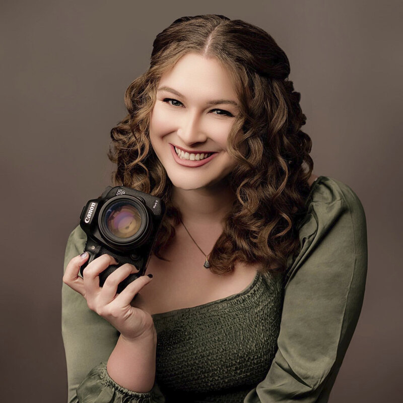women holding camera and smiling at the camera with a green top on 