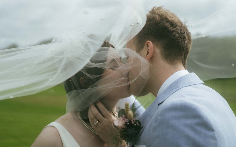 A bride and groom under a veil having an intimate kiss during post ceremony couple photoshoot. 
