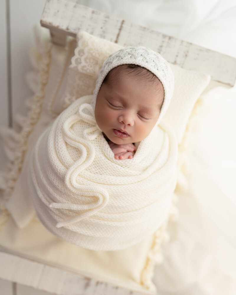 Elegant all-white newborn portrait with a textured wrap and lace bonnet, captured in Paris, Ontario.