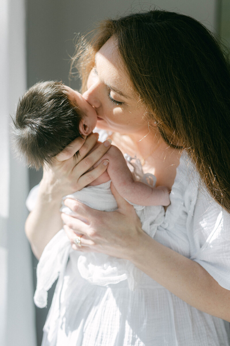 women kissing cheek of newborn baby in home with sunlight coming through the windows knoxville tennessee newborn photographer