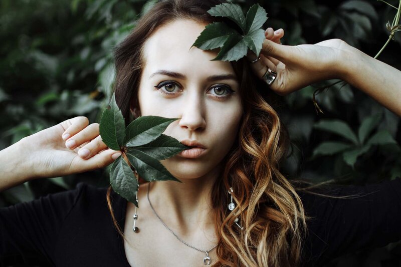 A close-up of a woman with long, wavy hair, holding green leaves near her face, exuding a natural and serene look. This image is for Debra LeClair's Embodied Style services.