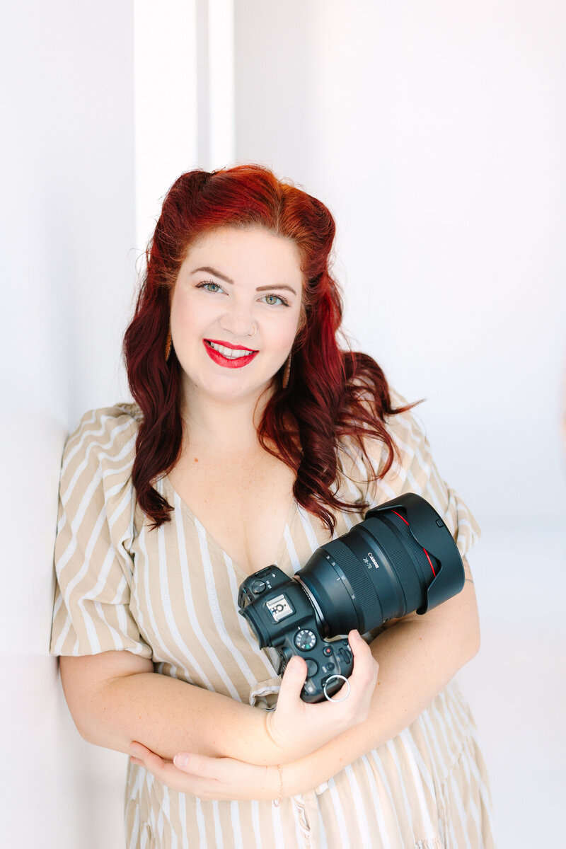 Portrait of Lelia Angelique, a wedding photographer, smiling while holding a camera in a bright and airy setting.