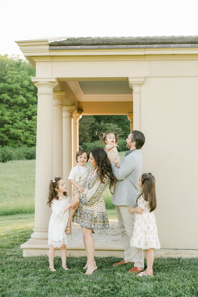 Family of six with young children in neutral clothing posing in front of pillared building  at Winterthur Estate at sunset