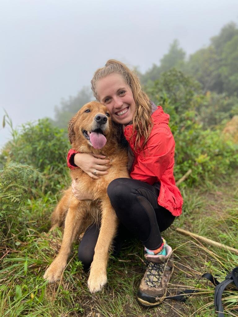 Girl smiling holding her golden retriever during a hike