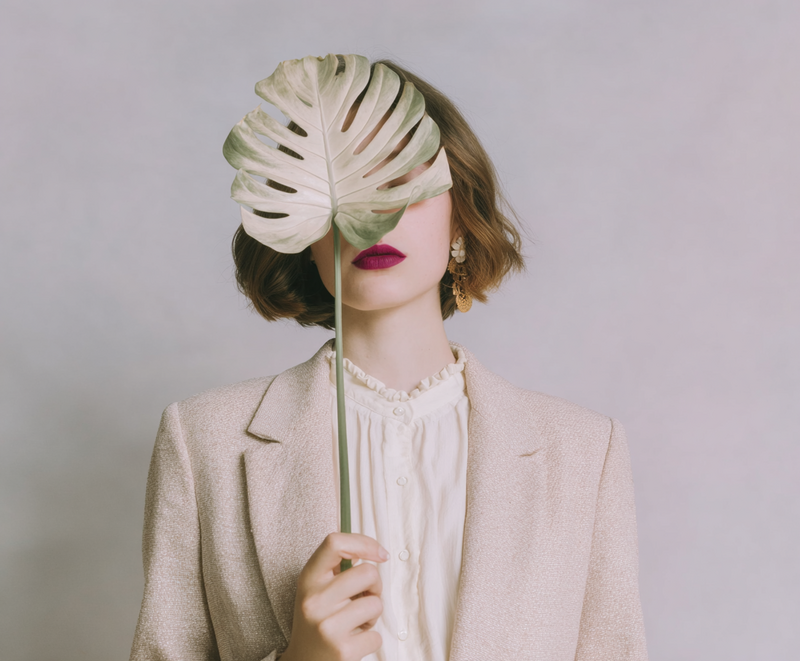 Woman in soft knitwear holding a script page in front of her face, surrounded by gold rings, capturing the power of voice, mystery, and the first step of self-expression.
