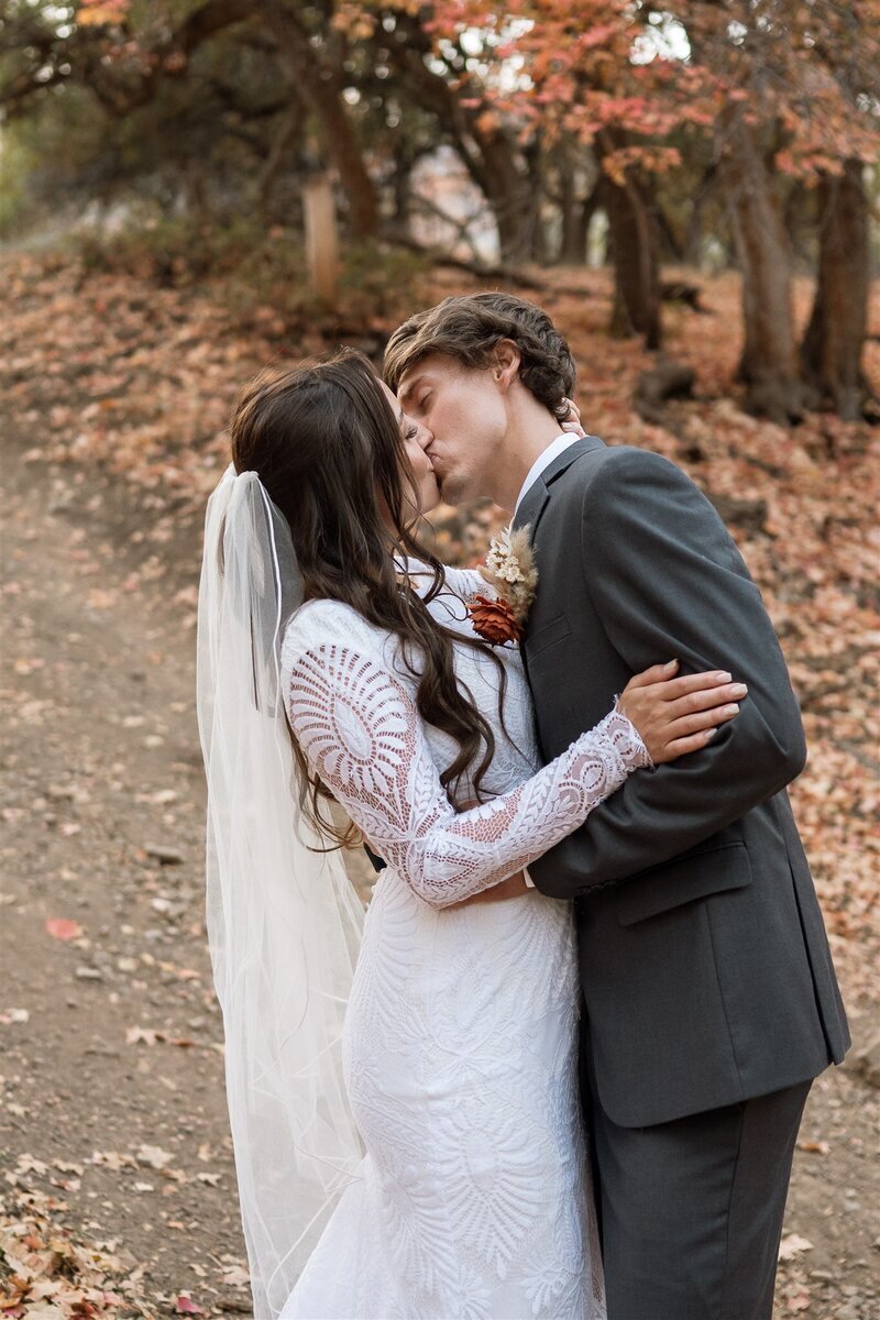 Married couple kissing with fall leaves in the background.