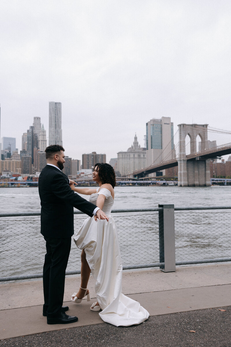 Newlywed couple sharing a romantic moment by the Brooklyn waterfront with the Brooklyn Bridge and NYC skyline in the background