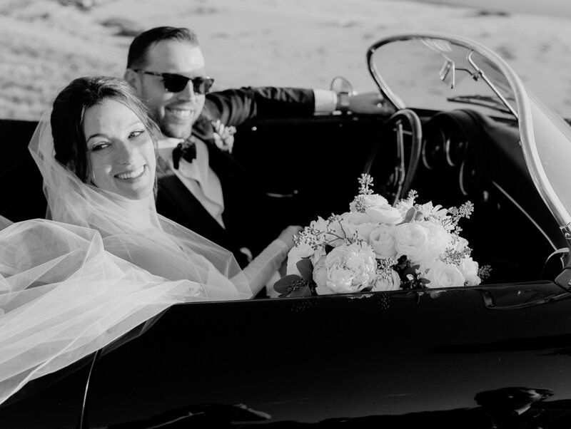black and white wedding image of couple in vintage black porshe