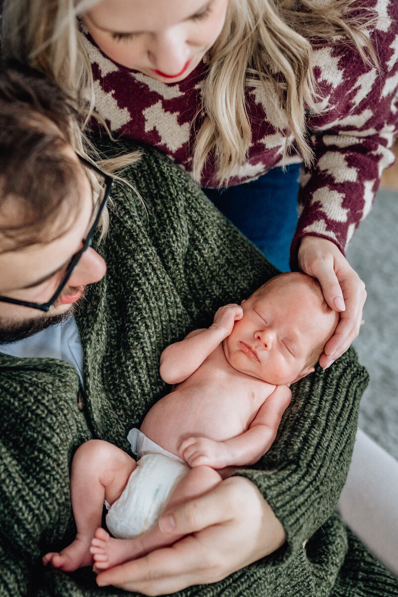 A close-up shot of a newborn baby being held by a parent, with another parent lovingly looking down.