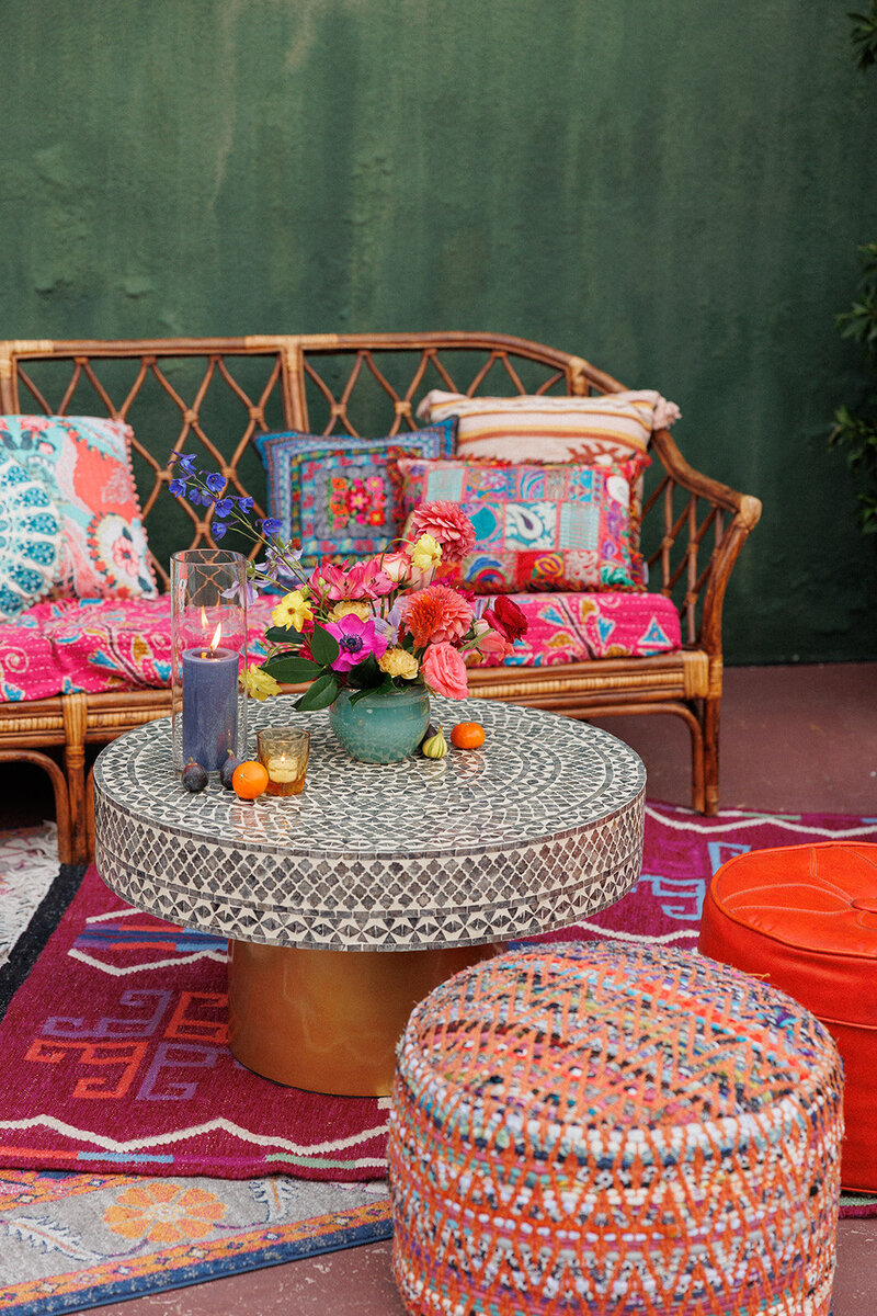 Colorful and eclectic party lounge featuring a bamboo sofa, embroidered fabric pillows, a mosaic stone coffee table, and colorful flowers and patterned rugs.
