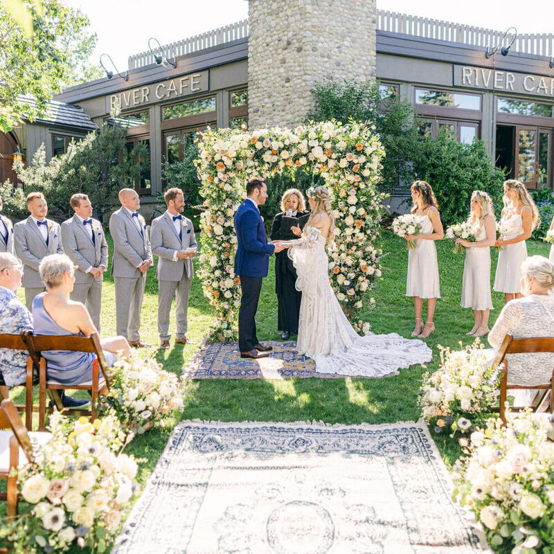 This beautiful outdoor ceremony at River Café in downtown Calgary captures the bride and groom surrounded by nature, celebrating their special day in an elegant setting.