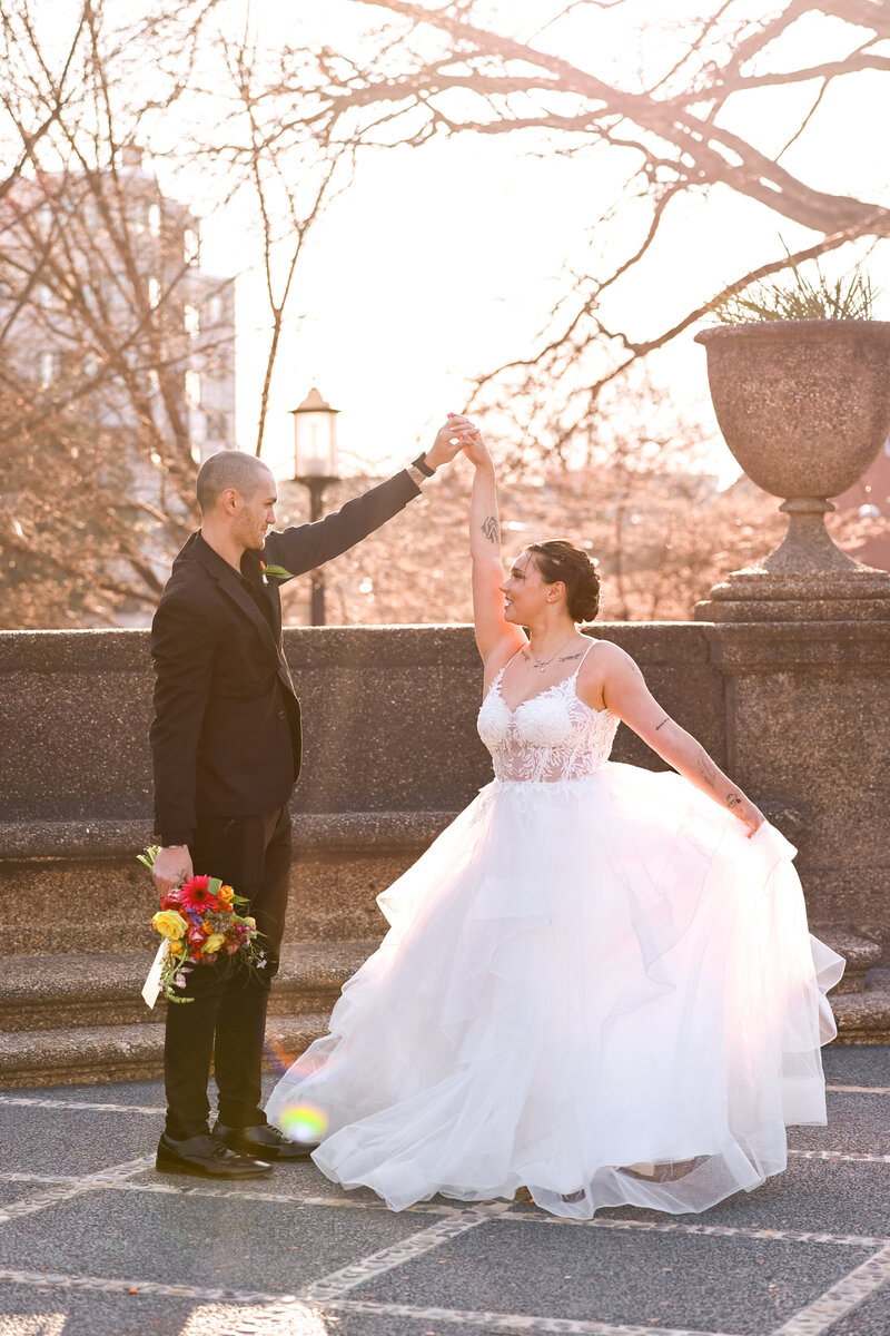 A groom with his arm up twirling his bride while holding a bouquet of flowers.