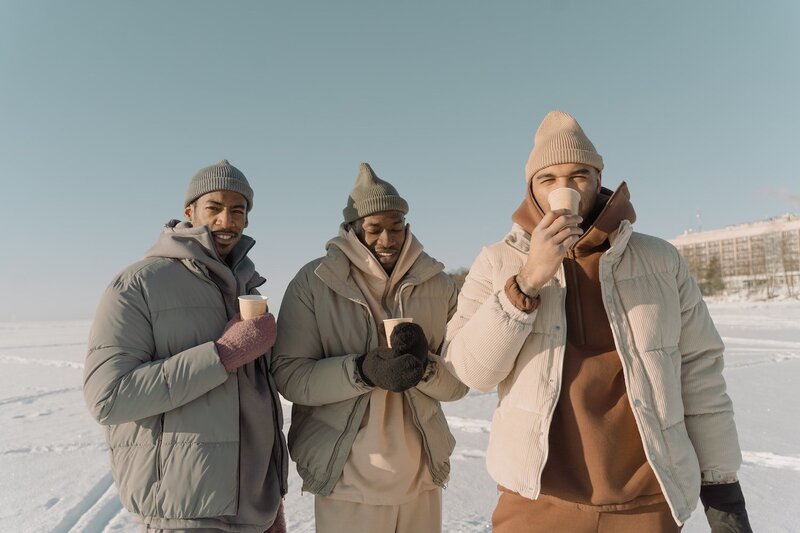 three happy men with coffees surrounded by show and winter