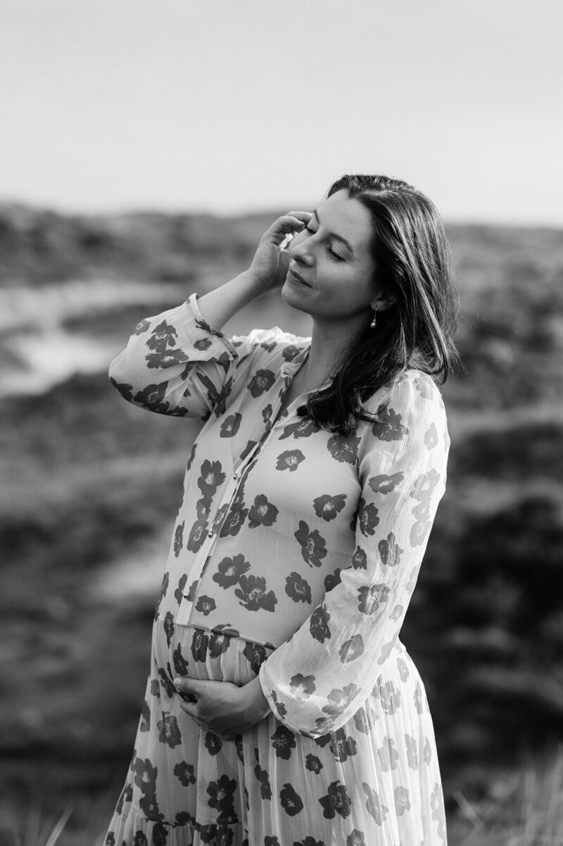 Zwangere vrouw poseert in de duinen en doet haar hand door haar haren