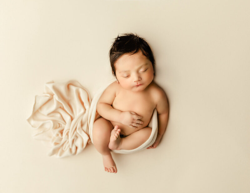 Newborn baby lying on a knitted blanket with soft textures and neutral colours, photographed in natural, timeless light.