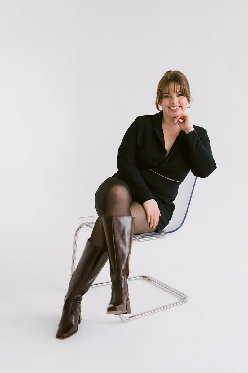 woman sitting in a clear chair with one hand rested under her chin and the other rested across her lap