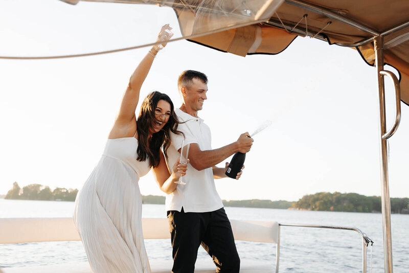 Engaged couple pops champagne on deck of yacht in Minnesota