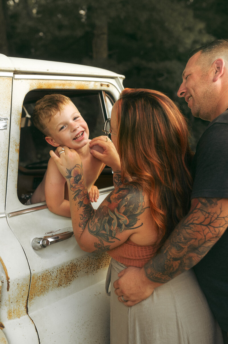 A mother and father sharing a kiss against a white picket fence while holding their baby boy. 