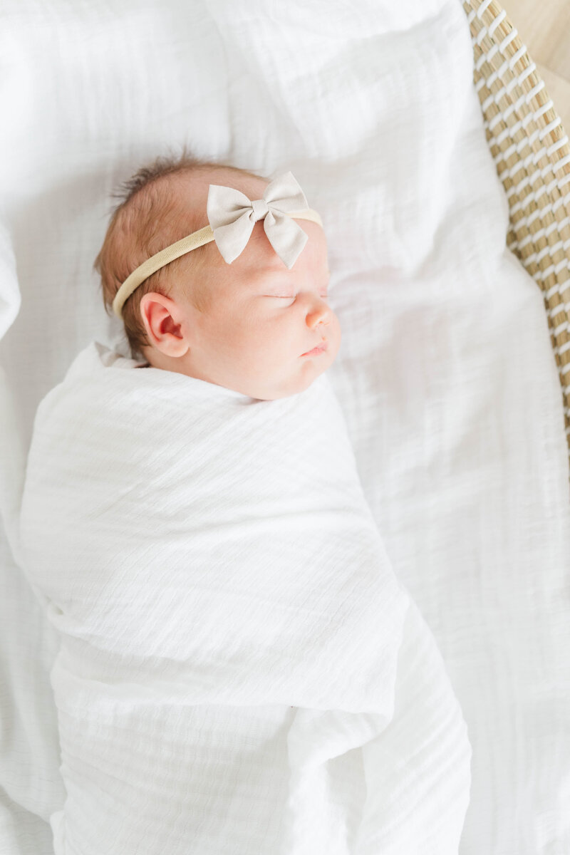 A peaceful moment of a swaddled newborn resting in a light white blanket, with gentle sunlight illuminating their face
