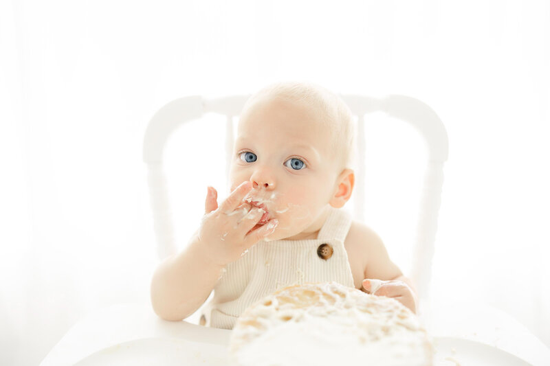 1st birthday cake smash session of baby eating cake in high chair in Northern Virginia