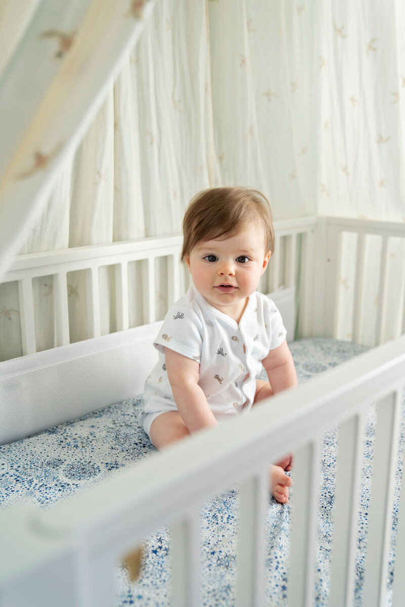 7 month old baby girl sitting in her cot during an at home photo shoot in Fulham