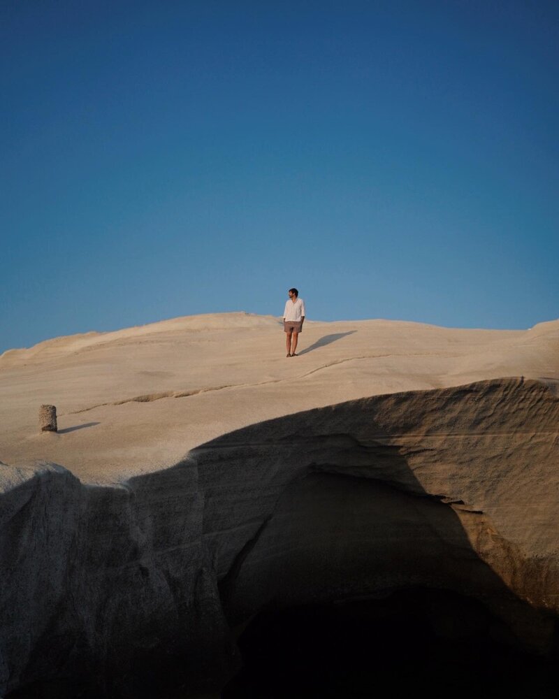 Photo of a person walking along a mountain landscape with blue sky in the background