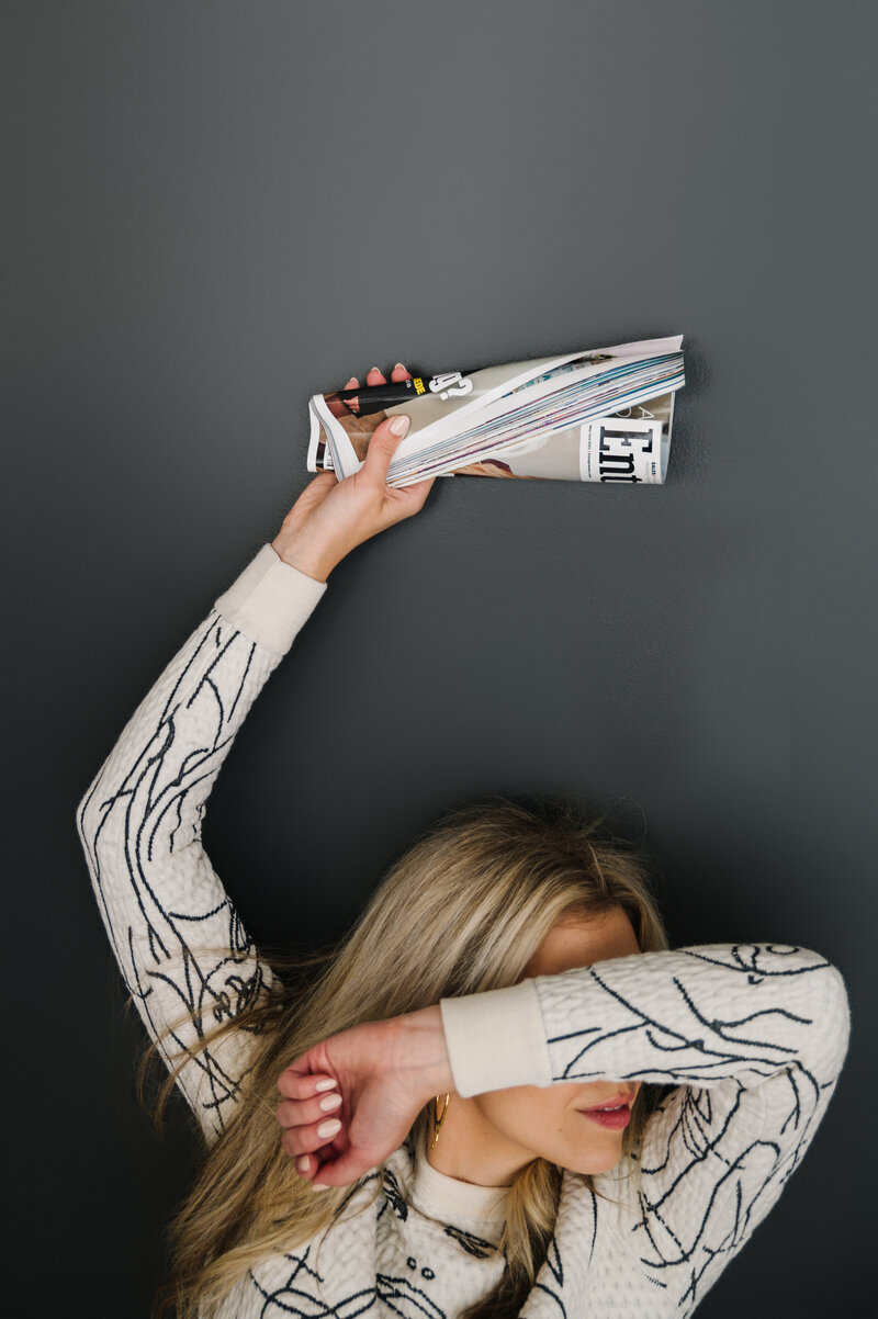 Sarah Klongerbo holding a newspaper above her head and covering her face with her arm