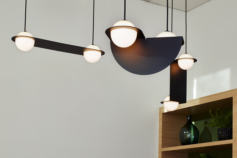 Interconnected globe pendant light fixtures hanging from the ceiling in front of a wood shelf containing a decorative green vase and a plant