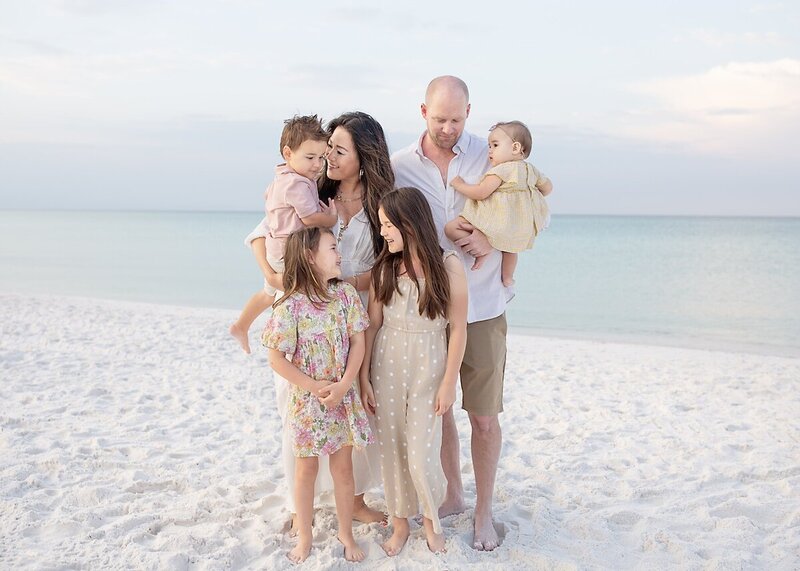 A family os 6 smiles at each other and poses on 30a beach